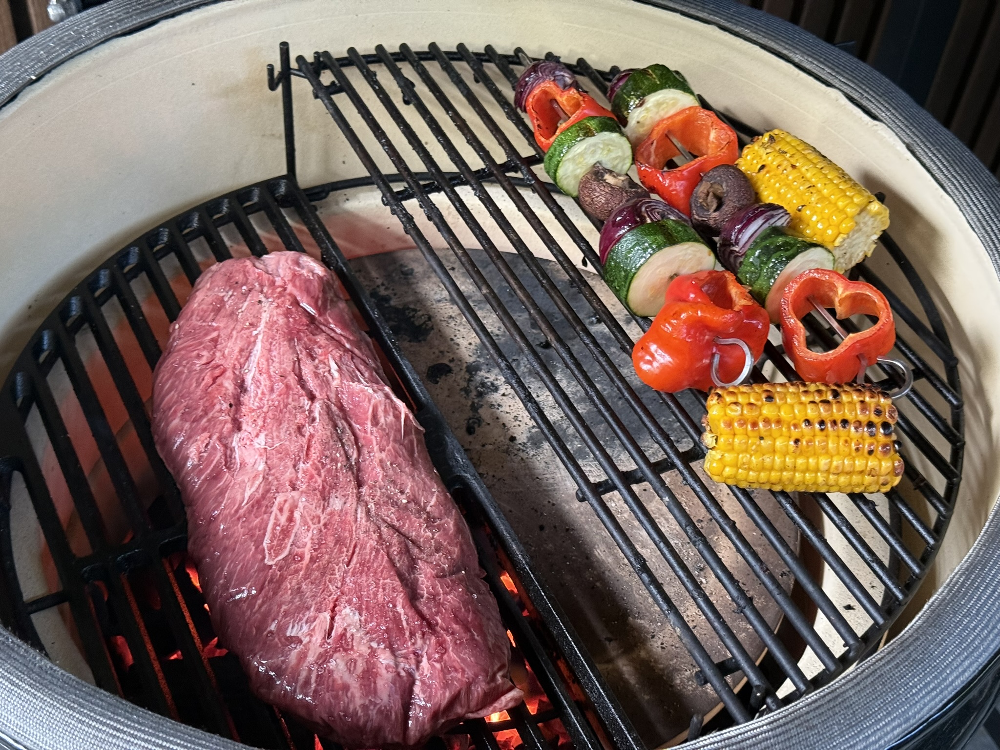 Twee zones op een kamado: steak direct boven open vuur, groente indirect boven de halve deflectorsteen
