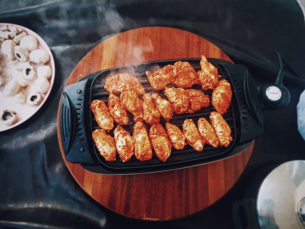 Kippenvleugels op een elektrische tafelgrill met thermostaatknop en snoer
