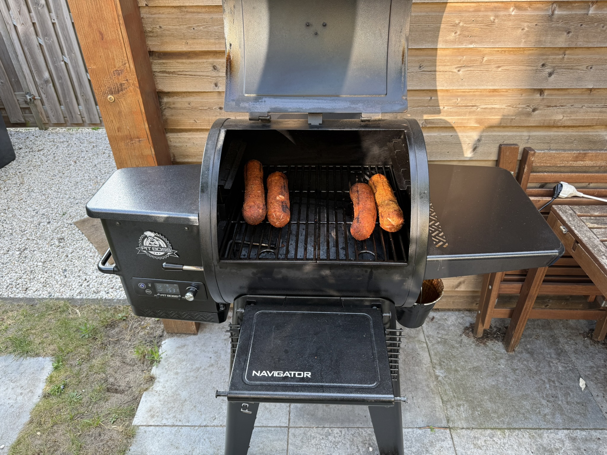 Pit Boss Navigator 550 pelletgrill met open deksel en vier grillworsten op het rooster