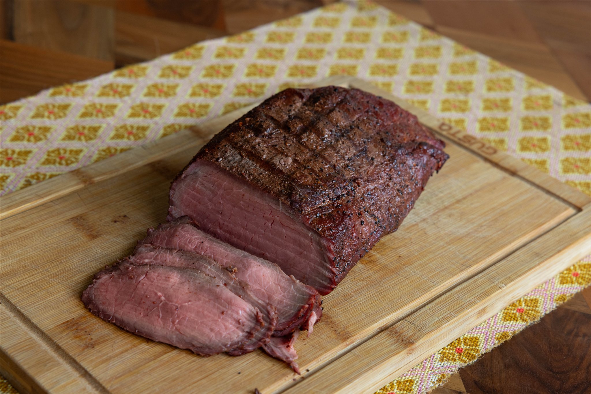 Aangesneden rosbief van de bbq met egaal rosé snijvlak, drie dunne plakken op de snijplank