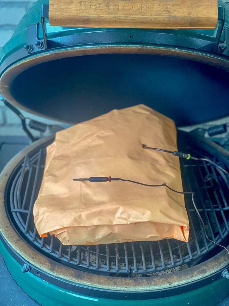 Brisket ingepakt in butcher paper op het rooster van een kamado, met twee voelerdraden erin