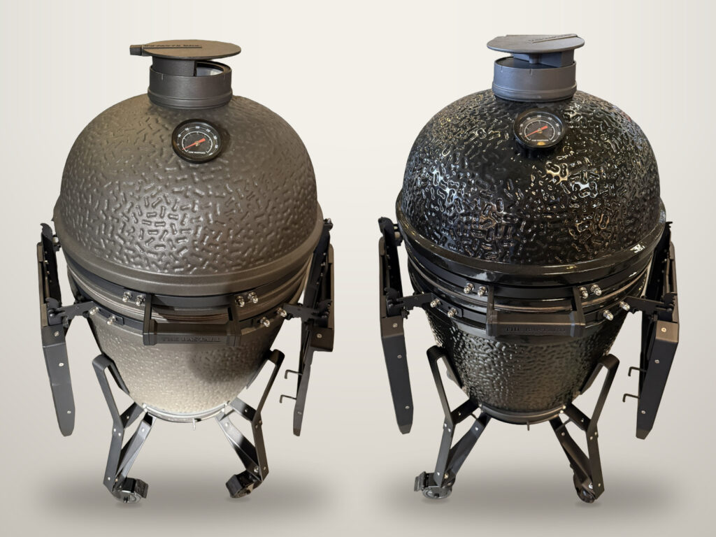 Twee The Bastard kamado's naast elkaar op een neutrale achtergrond: links de matte, ruwe uitvoering, rechts de hoogglans zwarte, allebei met gesloten deksel en ingeklapte zijtafels.